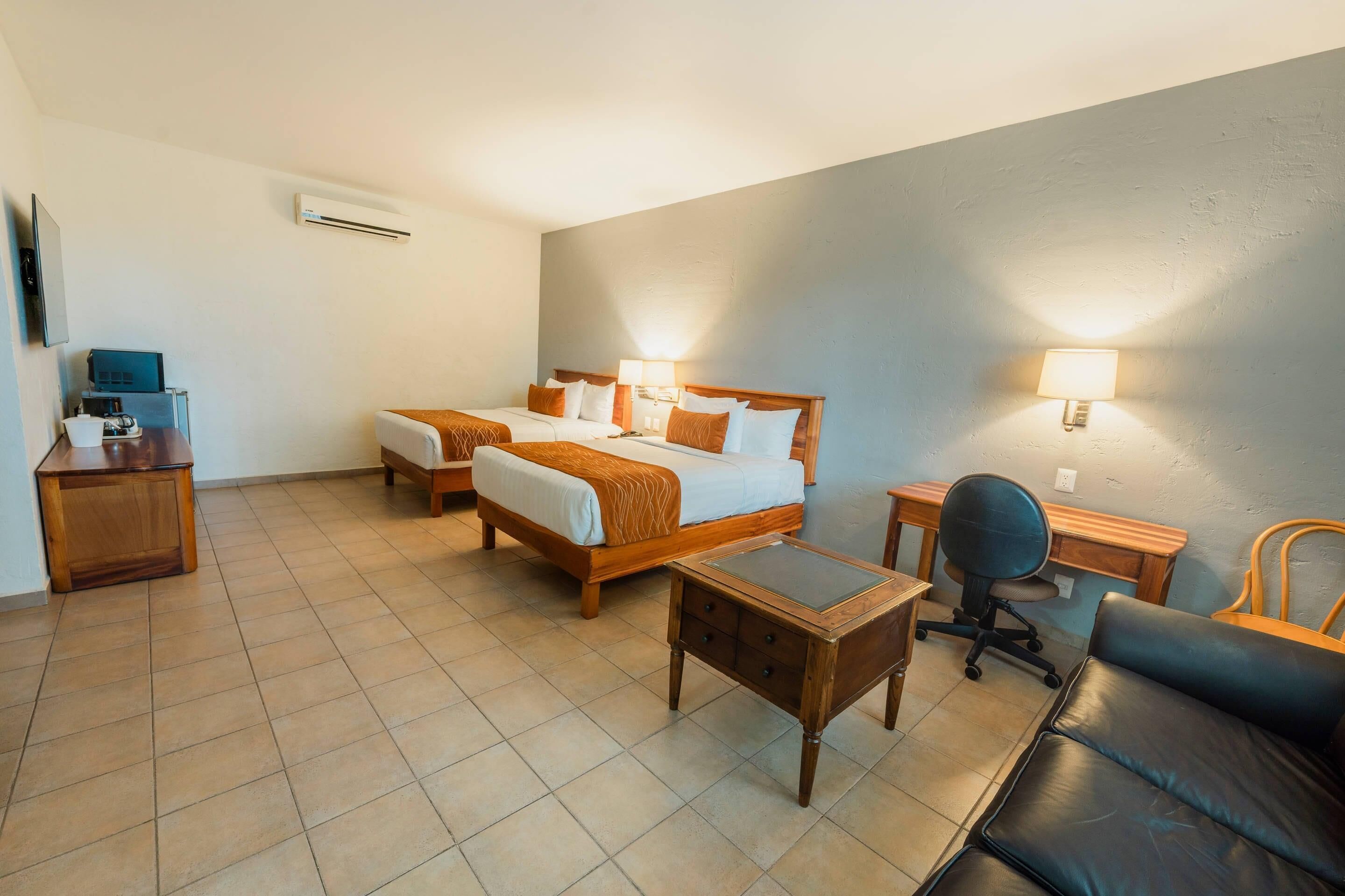 Ein Hotelzimmer mit zwei Betten, einem Schreibtisch, einem Stuhl, einem kleinen Tisch und einer Lampe.