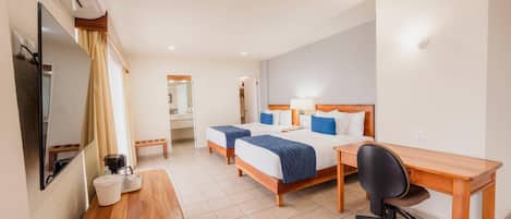 A hotel room with two beds, a desk, a chair, a TV, and a bathroom visible in the background.