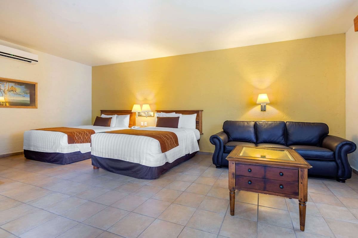 A hotel room with two beds, a sofa, a nightstand, and wall-mounted lamps.