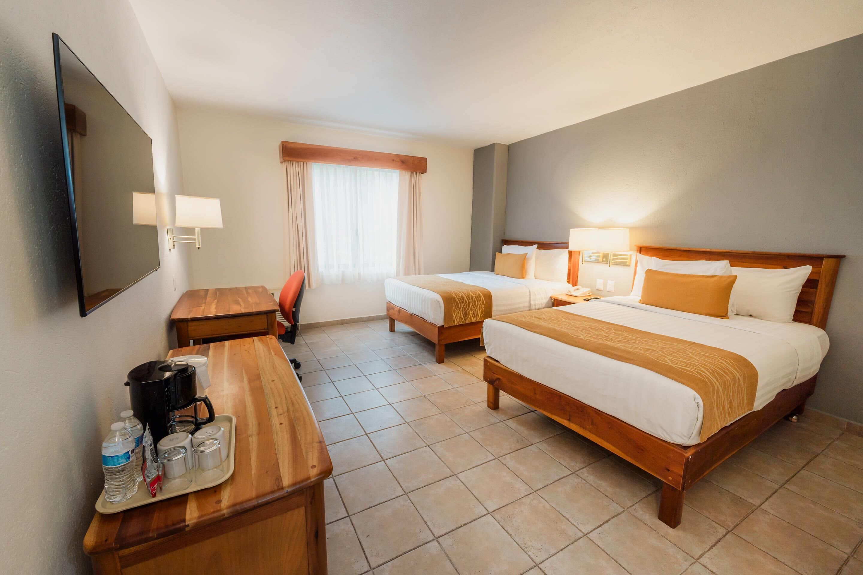 Una habitación de hotel con dos camas, un escritorio, una silla, un televisor y una ventana con cortinas.
