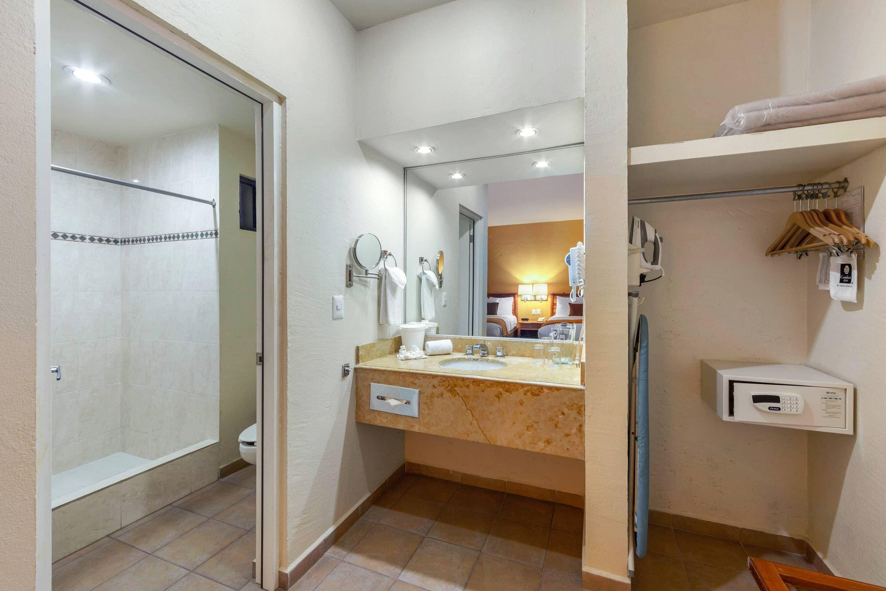 A bathroom with a shower, toilet, sink, mirror, towel rack, and a digital control panel.