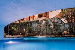 Una piscina con una cascada, un muro de piedra y un edificio con balcones.