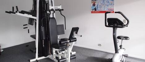 Ein Heimfitnessraum mit Kraftgerät, Crosstrainer und einem Poster an der Wand.