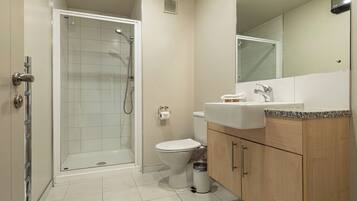 Un baño moderno con ducha de vidrio, inodoro, lavamanos con encimera de granito y armarios de madera.