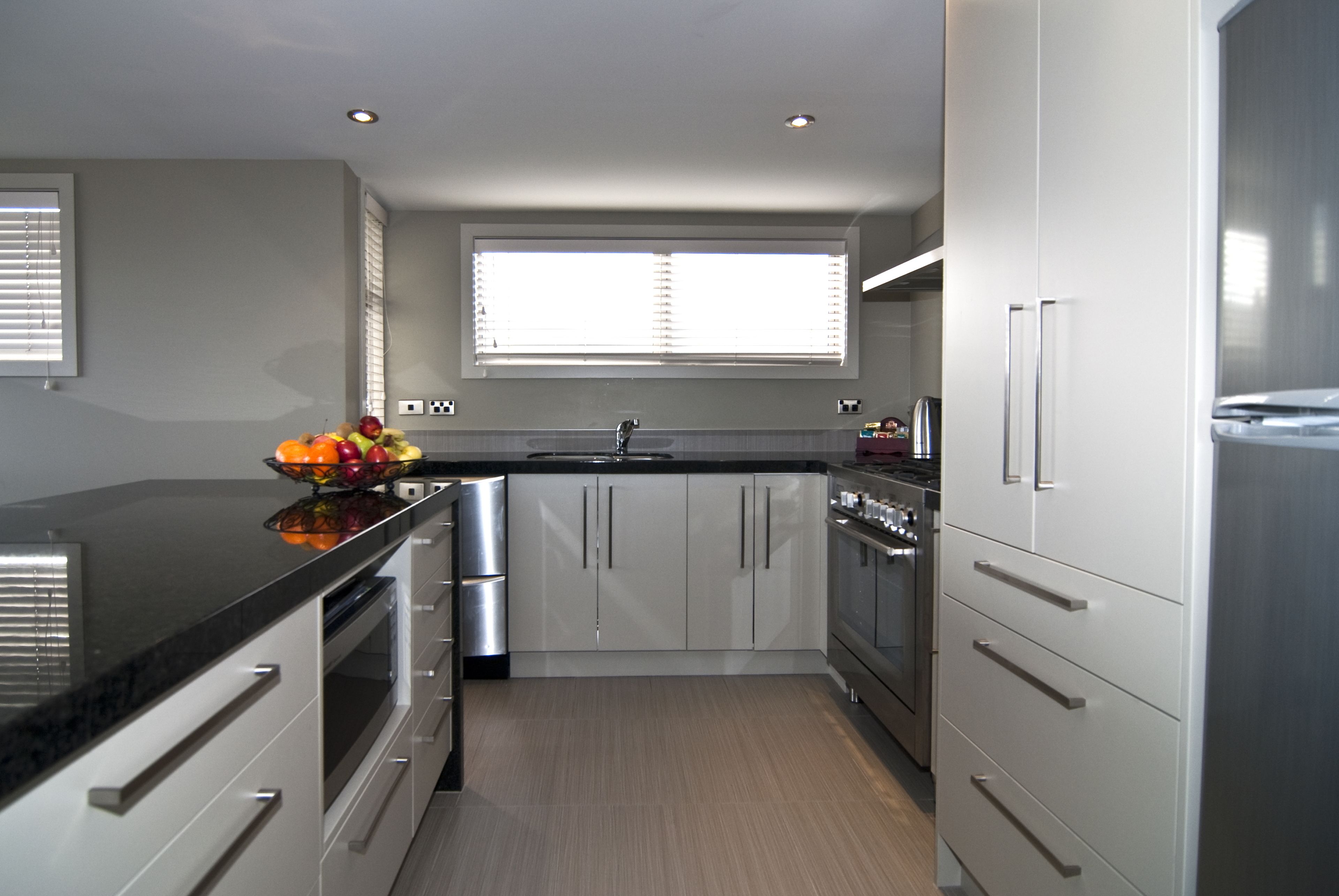 A modern kitchen with stainless steel appliances, a black countertop, and white cabinetry.