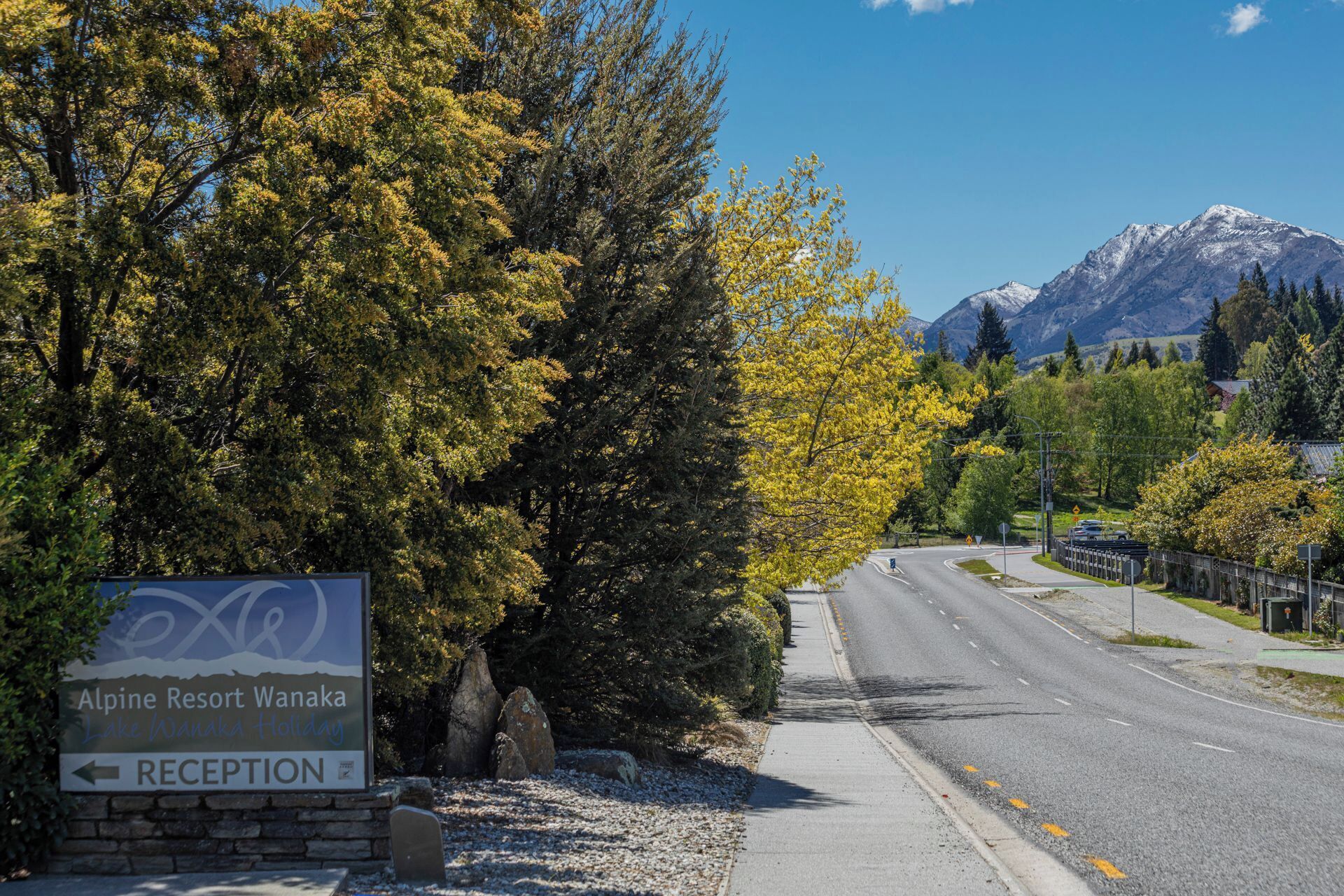 Una carretera que lleva al complejo turístico Alpine Resort Wanaika, con un cartel de recepción.