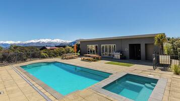 A modern outdoor pool area with two pools, a barbecue, and a view of snow-capped mountains.