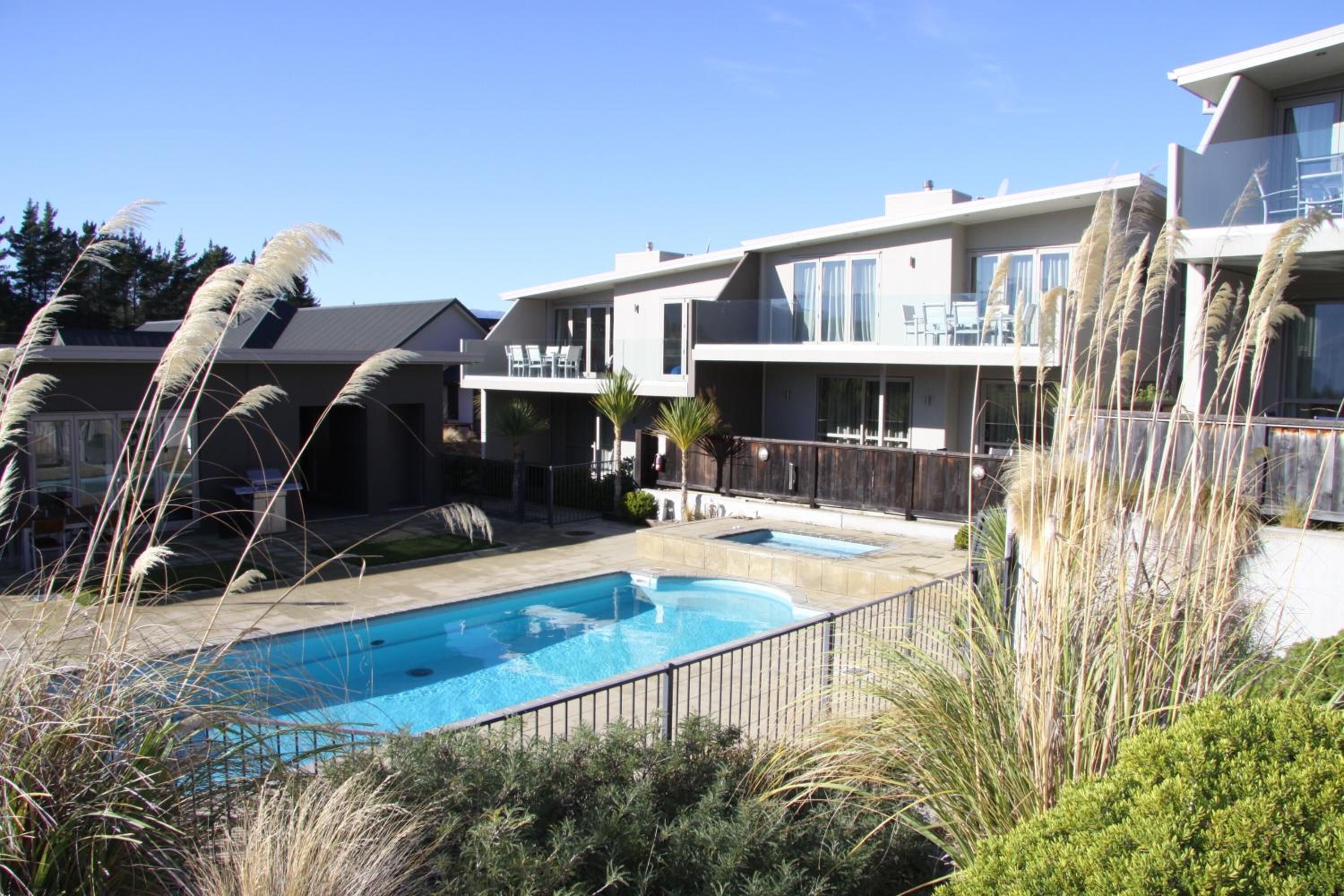 A modern residential building with a swimming pool, balconies, and a clear blue sky.
