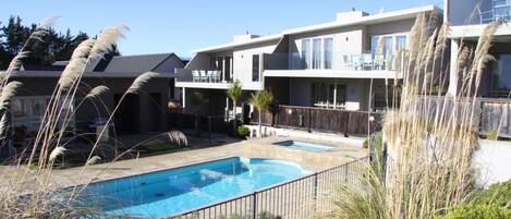 A modern residential building with a swimming pool, balconies, and a clear blue sky.
