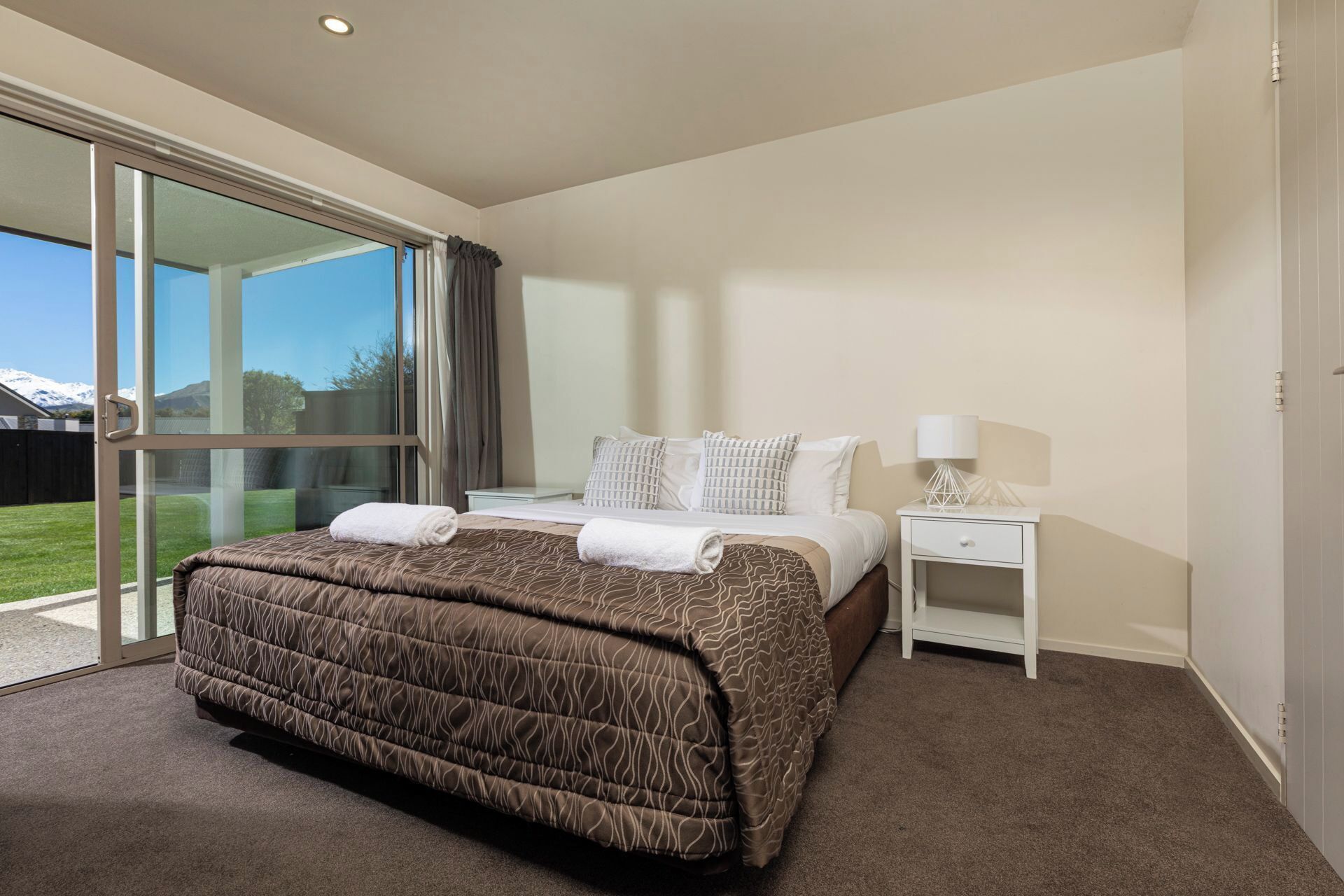 Habitación de hotel moderna con una cama grande, una mesita de noche con lámpara y una puerta corrediza de vidrio que da a un balcón.