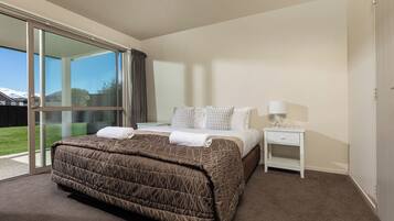 Habitación de hotel moderna con una cama grande, una mesita de noche con lámpara y una puerta corrediza de vidrio que da a un balcón.