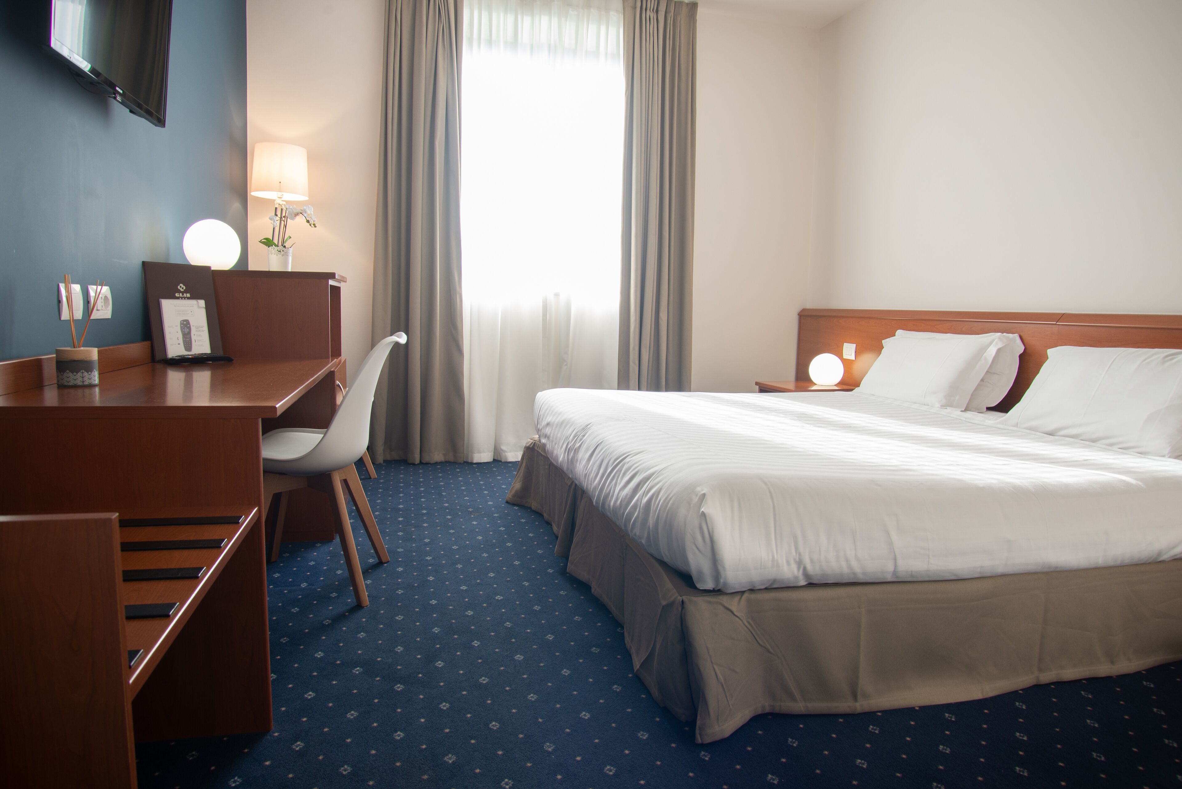 Hotellihuone, jossa on sänky, työpöytä, tuoli ja seinälle asennettu televisio.