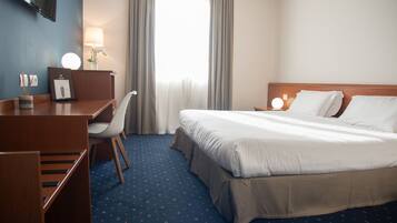 A hotel room with a bed, desk, chair, and a TV mounted on the wall.