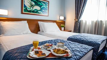 Camera d'albergo con due letti, un vassoio per la colazione con pasticcini, una tazza di caffè e un bicchiere di succo d'arancia.