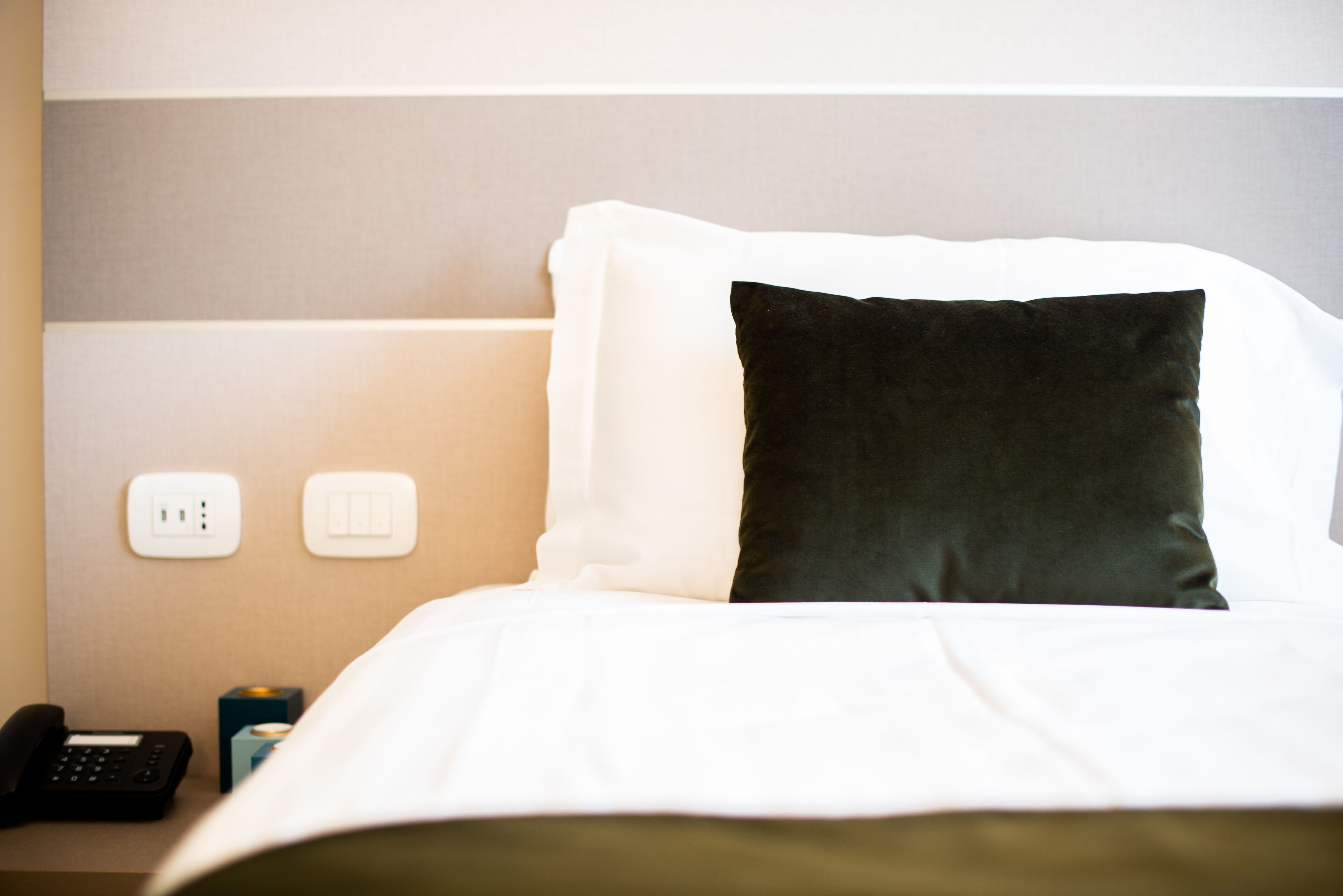 Una habitación de hotel con una cama bien hecha, un teléfono en la mesita de noche y un enchufe en la pared.
