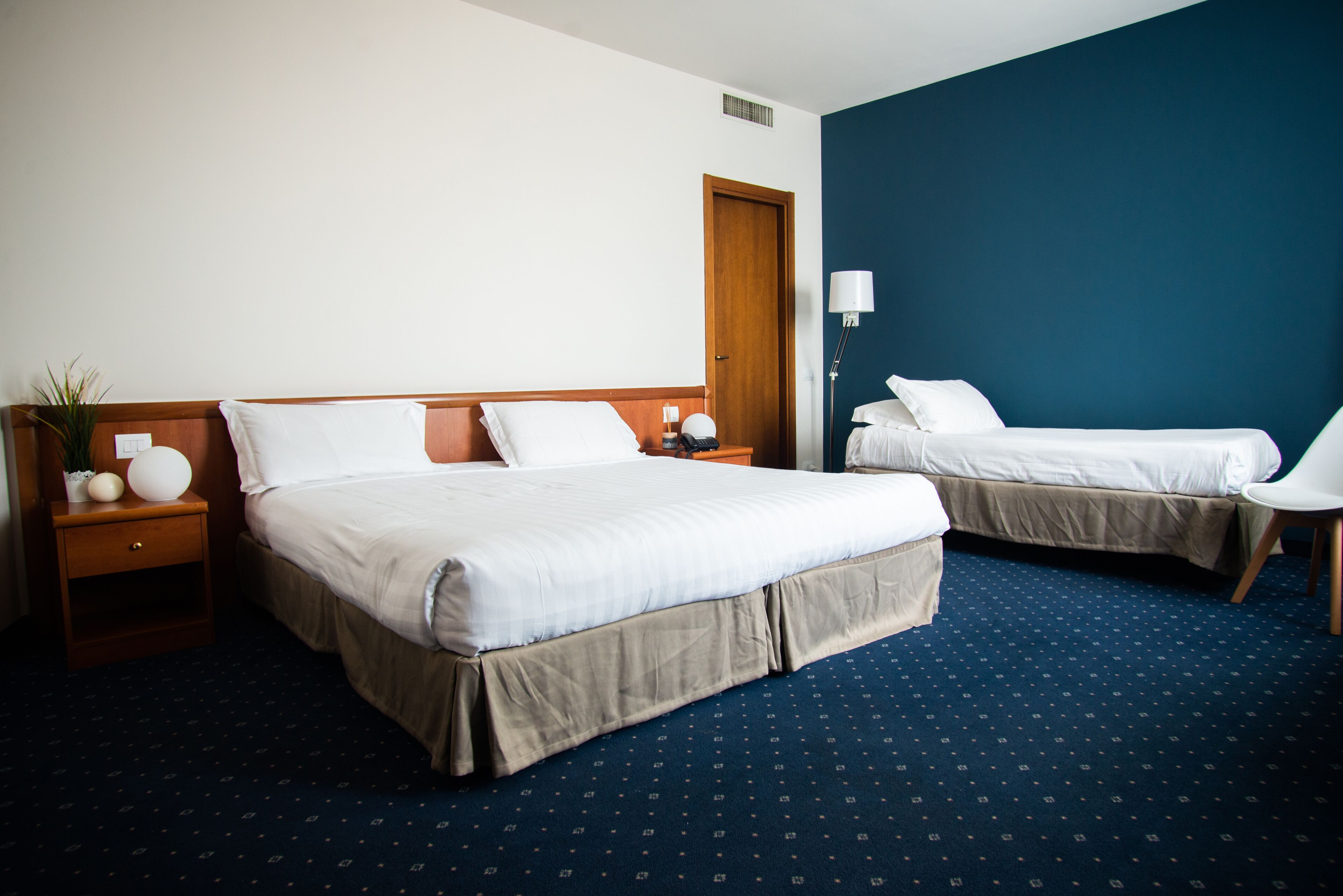 A hotel room with two beds, a nightstand, a lamp, and a chair.