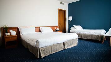 A hotel room with two beds, a nightstand, a lamp, and a chair.