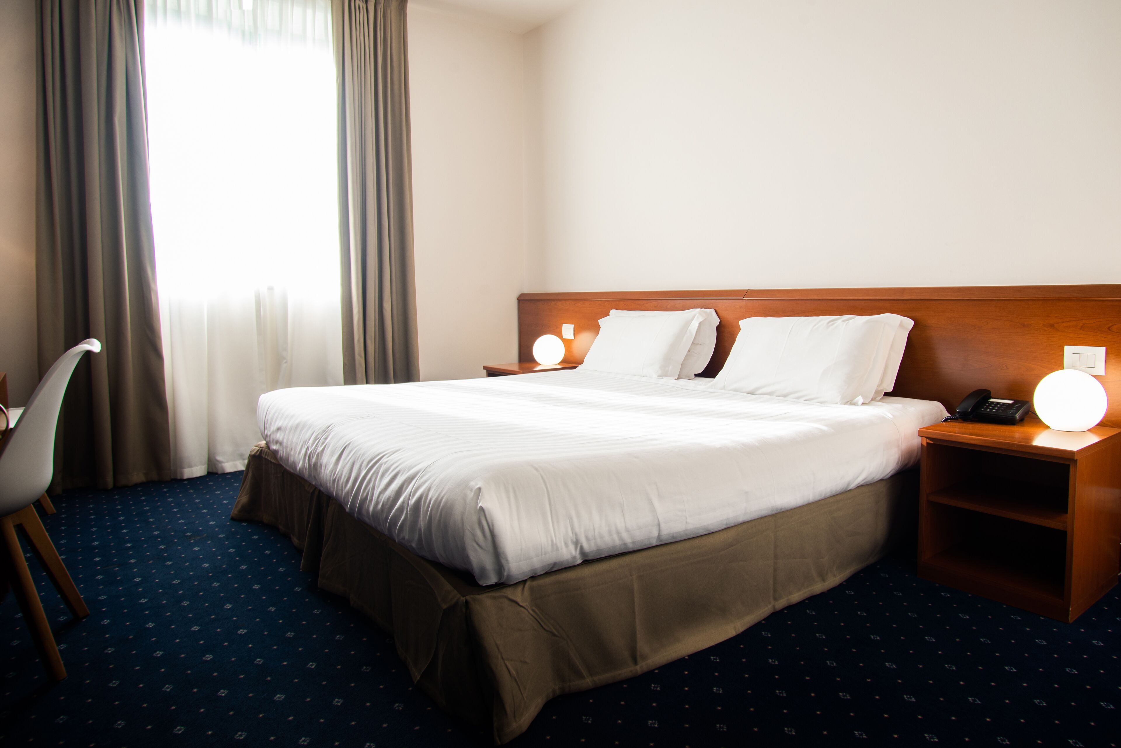 A hotel room with a large bed, a desk, and a chair. There are two bedside tables with lamps.