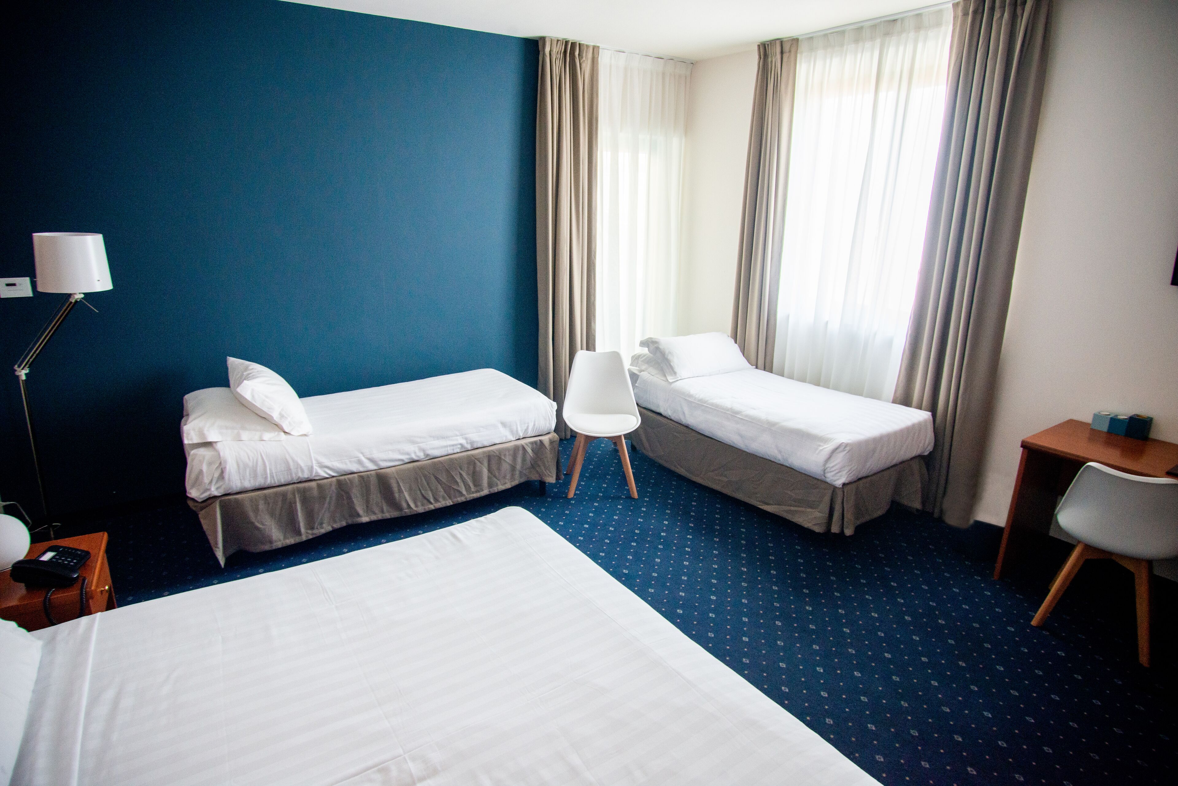 A hotel room with two single beds, a desk, a chair, a lamp, and a telephone on a nightstand.