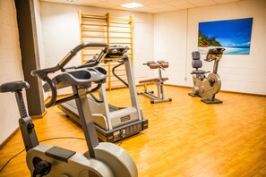 A gym with exercise equipment, wooden flooring, and a painting on the wall. - Hotel Glis (San Mauro Torinese)