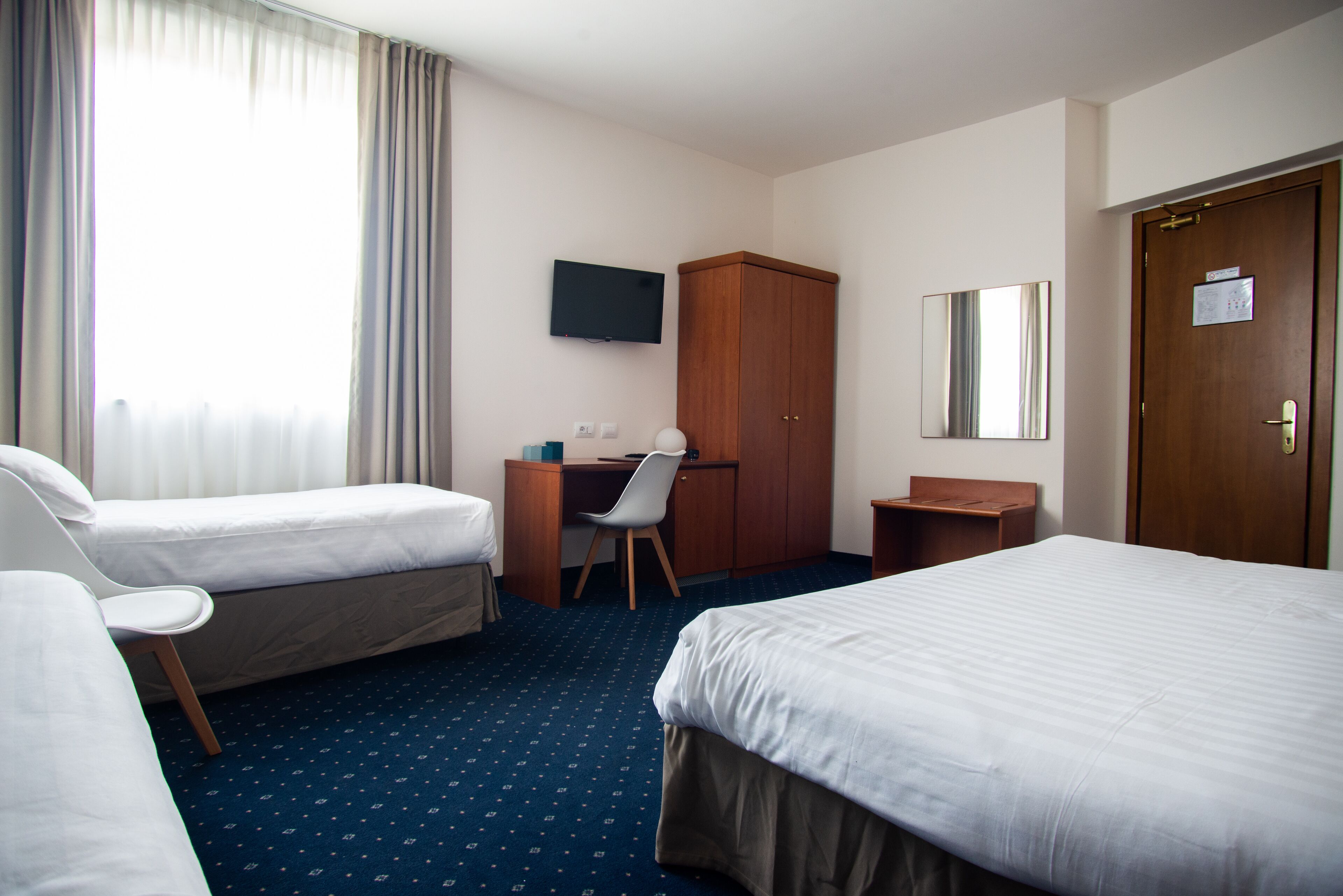 Camera d'albergo con due letti, una scrivania, una sedia, una televisione, un armadio e una porta con un cartello.