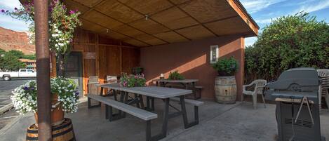 Terrassa exterior amb taules de picnic, una barbacoa i plantes en testos.