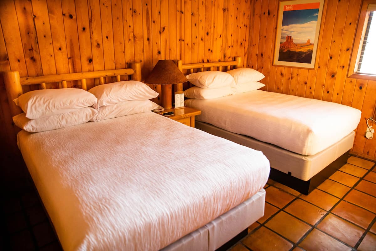 A room with two beds, wooden walls, a nightstand with a lamp, and a poster on the wall.