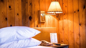 A wooden-paneled room with a bed, a nightstand, a lamp, a telephone, and a menu.