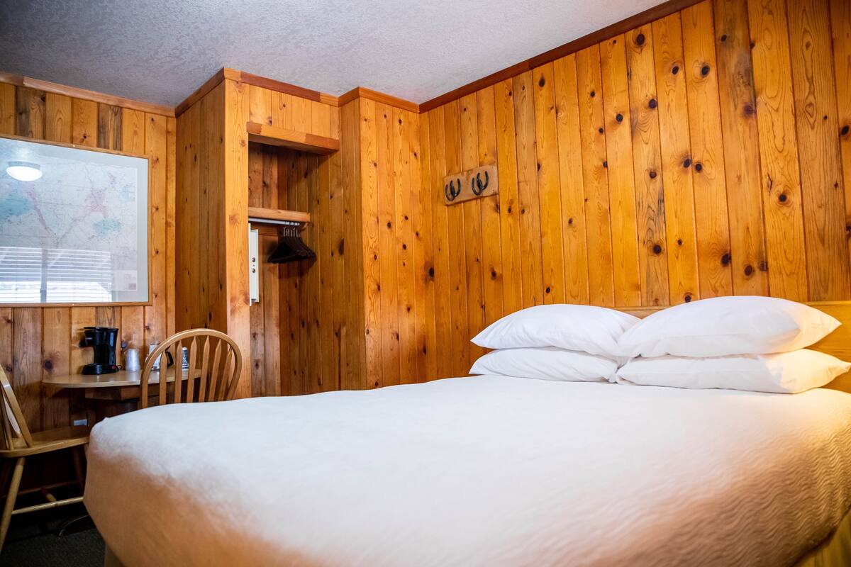 A wooden-paneled room with a bed, a desk, and a map on the wall.