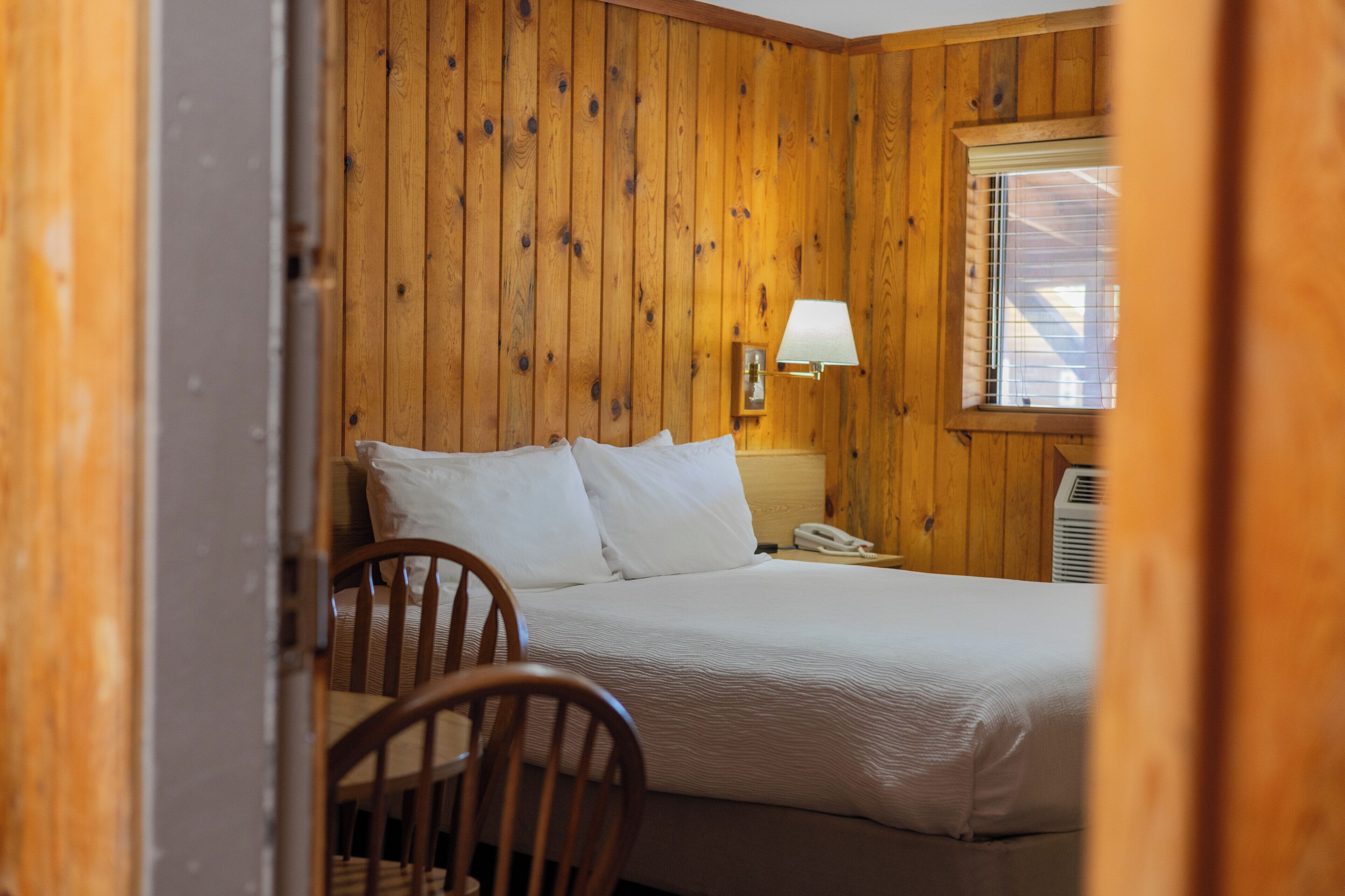 A wooden-paneled room with a bed, a chair, a bedside lamp, and a telephone.
