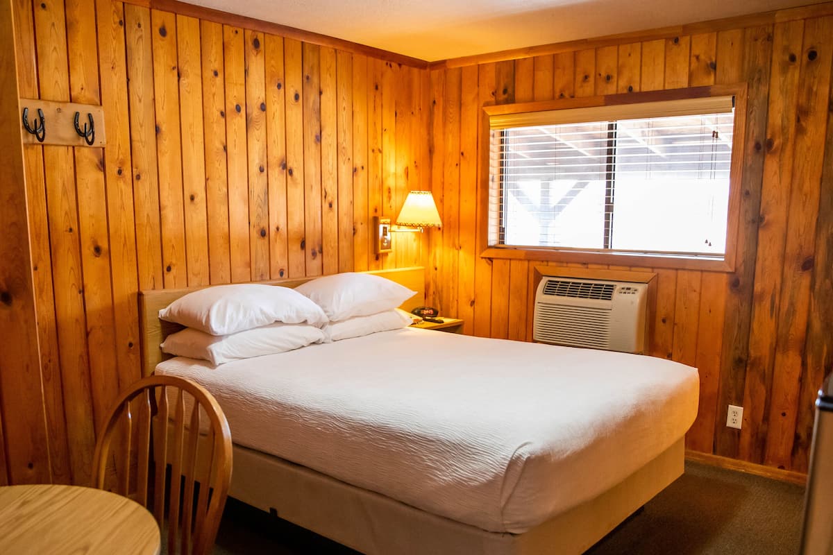 A wooden-paneled room with a bed, a table, and a chair.
