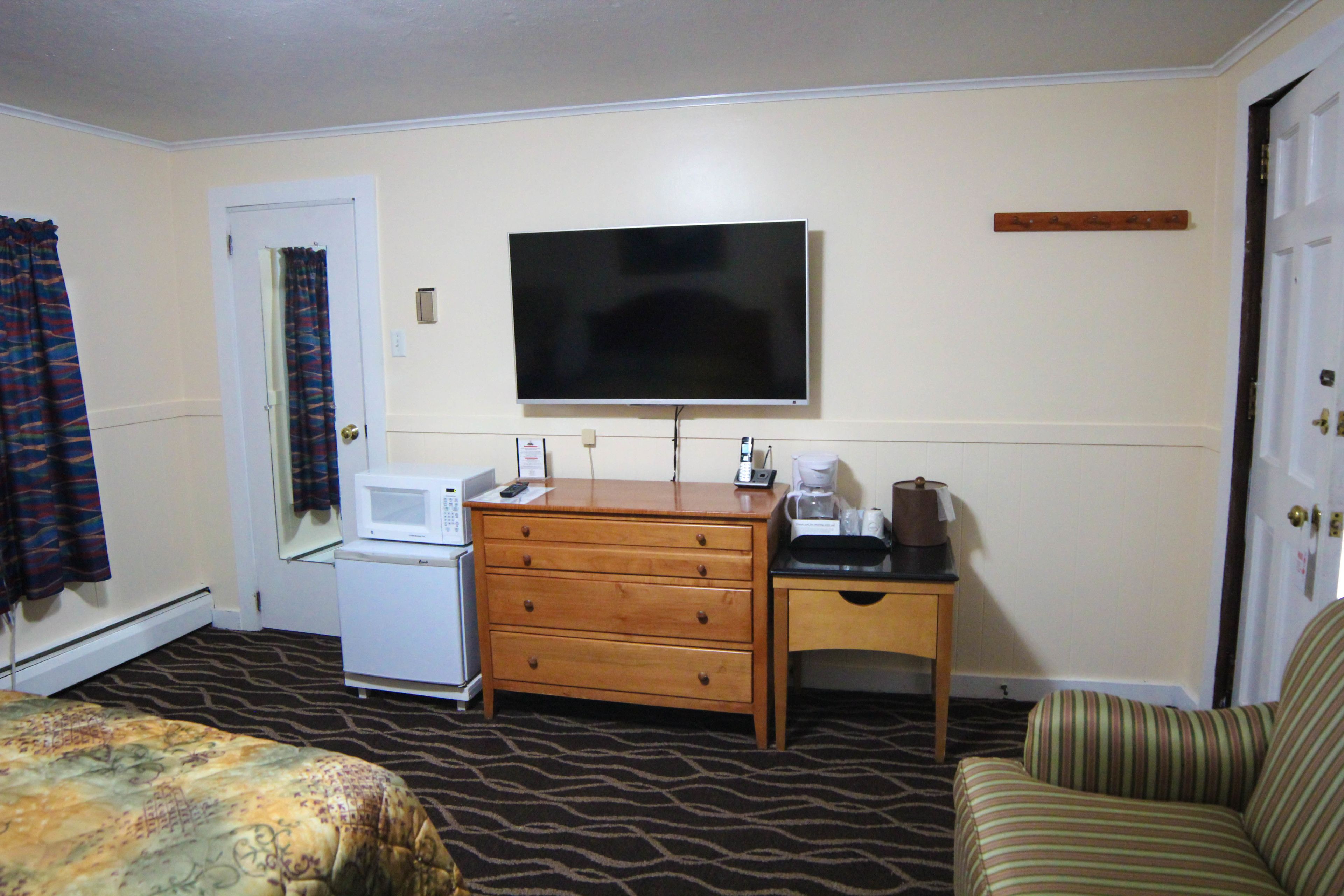 Habitación de hotel con cama, cómoda, televisor, microondas, cafetera y un sillón a rayas.