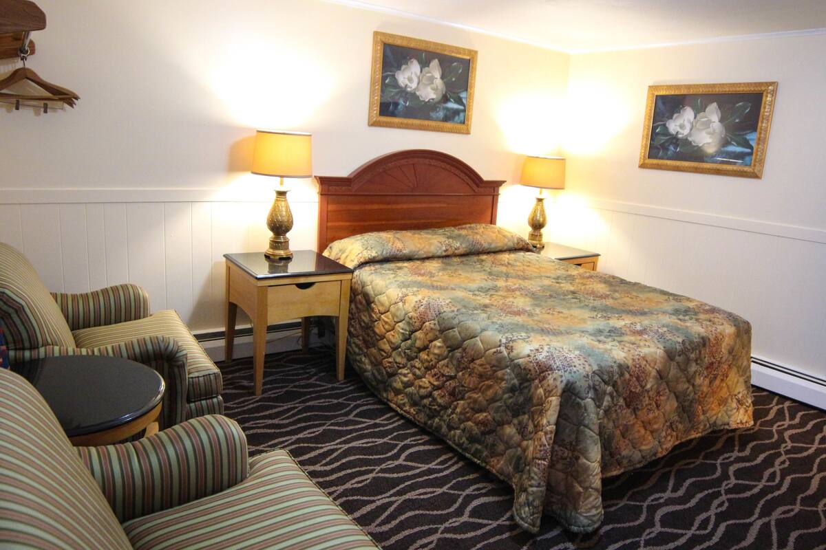 Une chambre d’hôtel avec un lit, deux tables de chevet avec des lampes, un canapé à rayures et deux tableaux accrochés au mur.