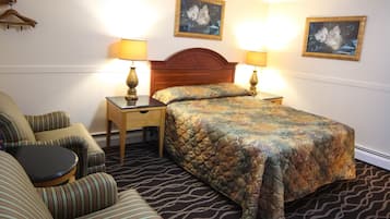 A hotel room with a bed, two bedside tables with lamps, a striped sofa, and two wall-mounted paintings.