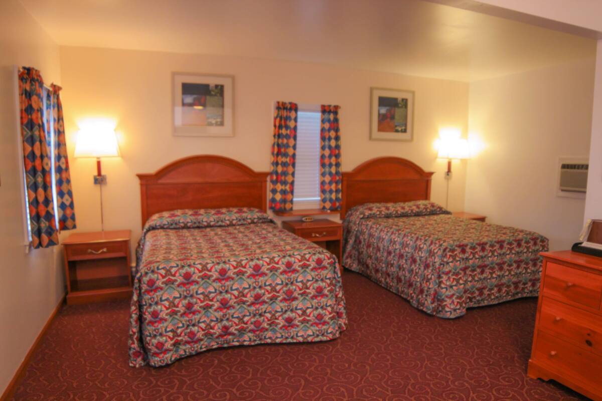Une chambre d’hôtel avec deux lits, une commode et deux lampes.