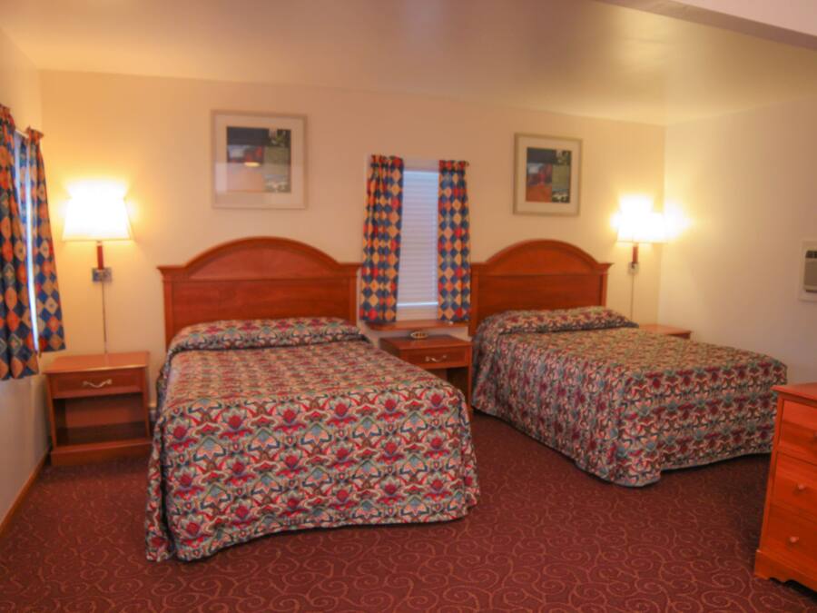 A hotel room with two beds, a dresser, and two lamps.
