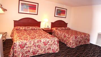 A hotel room with two beds, a nightstand, a lamp, and two framed pictures on the wall.