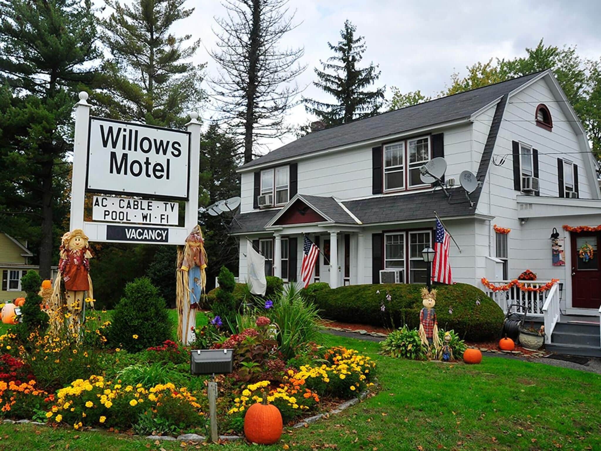 Casa blanca de dos pisos con un cartel que indica Motel Willows, que ofrece servicios como aire acondicionado, televisión por cable, piscina, Wi-Fi y televisión.