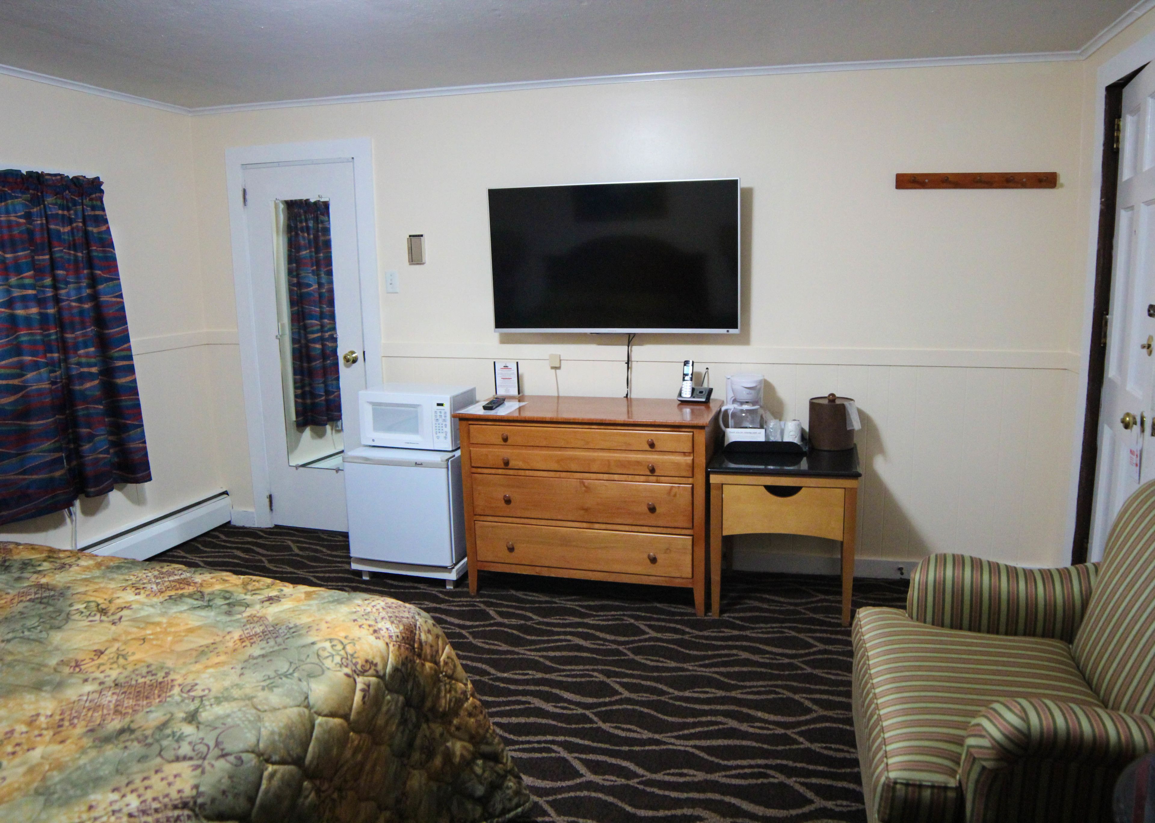 A hotel room with a bed, a dresser, a microwave, a television, a coffee maker, and a chair.