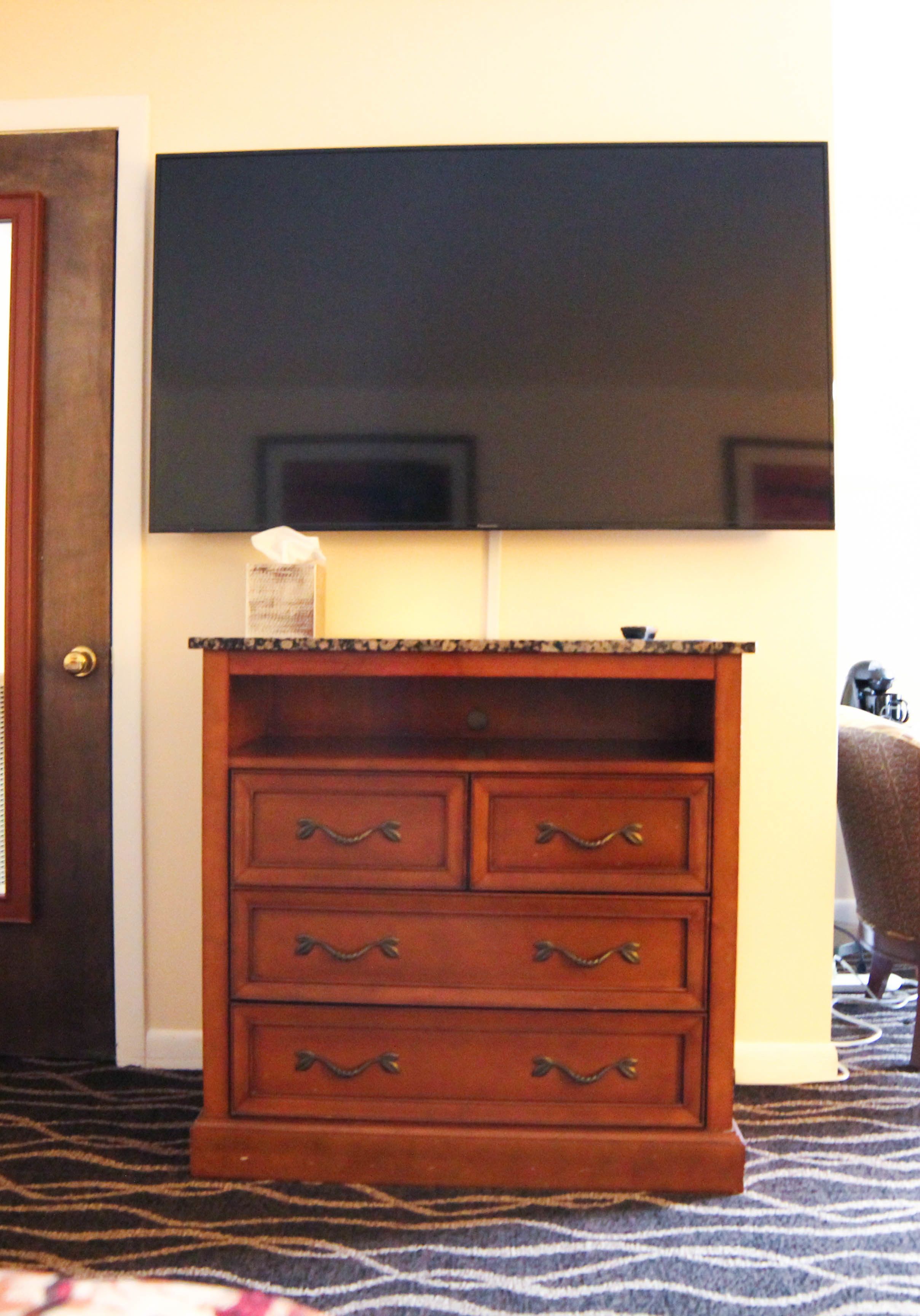 A wooden dresser with drawers and a mirror above it, positioned in a room with a patterned carpet.