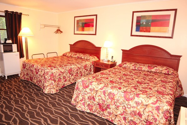 A hotel room with two beds, a desk, a lamp, and a refrigerator.