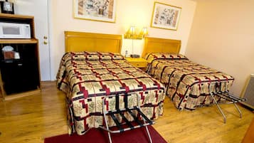 A hotel room with two beds, a microwave, a small table with a lamp, and artwork on the walls.