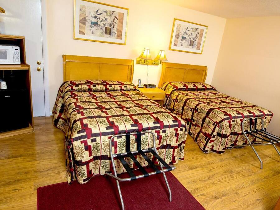 A hotel room with two beds, a microwave, a small table with a lamp, and artwork on the walls.