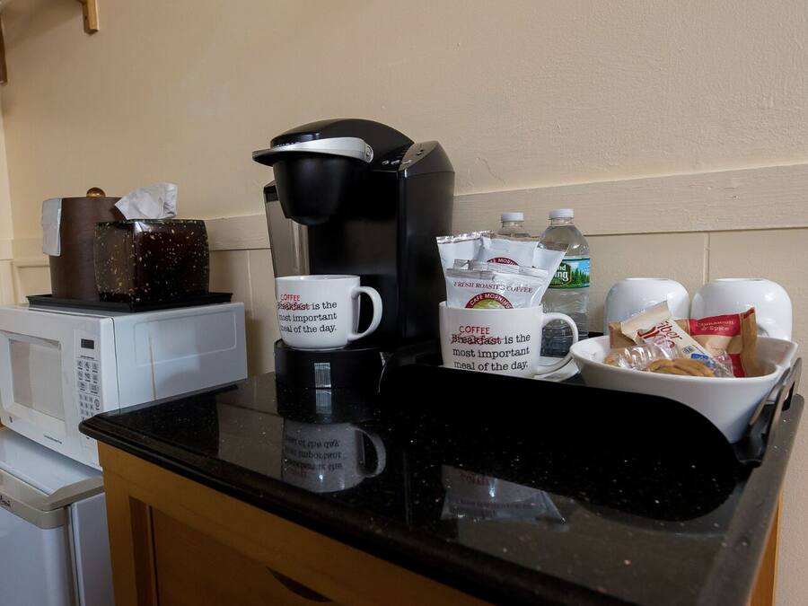 Una encimera de cocina con una cafetera, dos tazas con la palabra 'desayuno', una botella de agua y un bol de aperitivos.