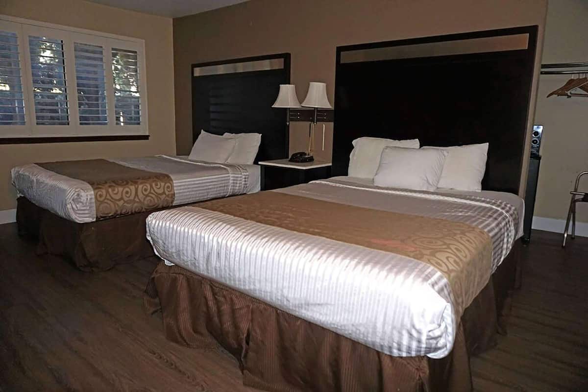 A hotel room with two beds, a nightstand with lamps, and a window with blinds.