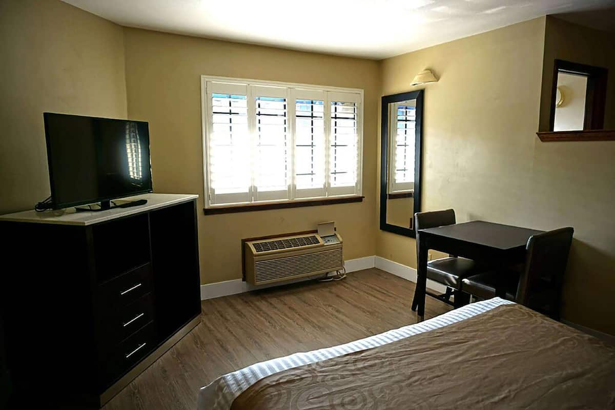 A hotel room with a bed, a desk, a chair, a TV, and a window with blinds.