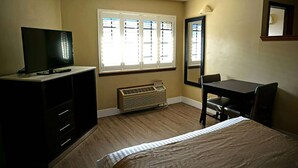 A hotel room with a bed, a desk, a chair, a TV, and a window with blinds. - Travelodge by Wyndham Concord (Concord)