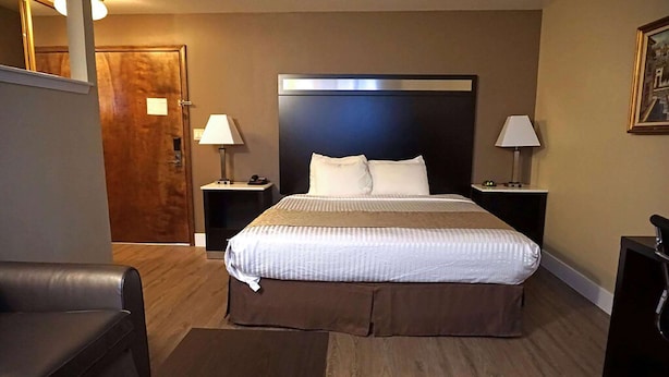 A hotel room with a large bed, two bedside tables with lamps, a wooden floor, and a leather chair. - Travelodge by Wyndham Concord (Concord)