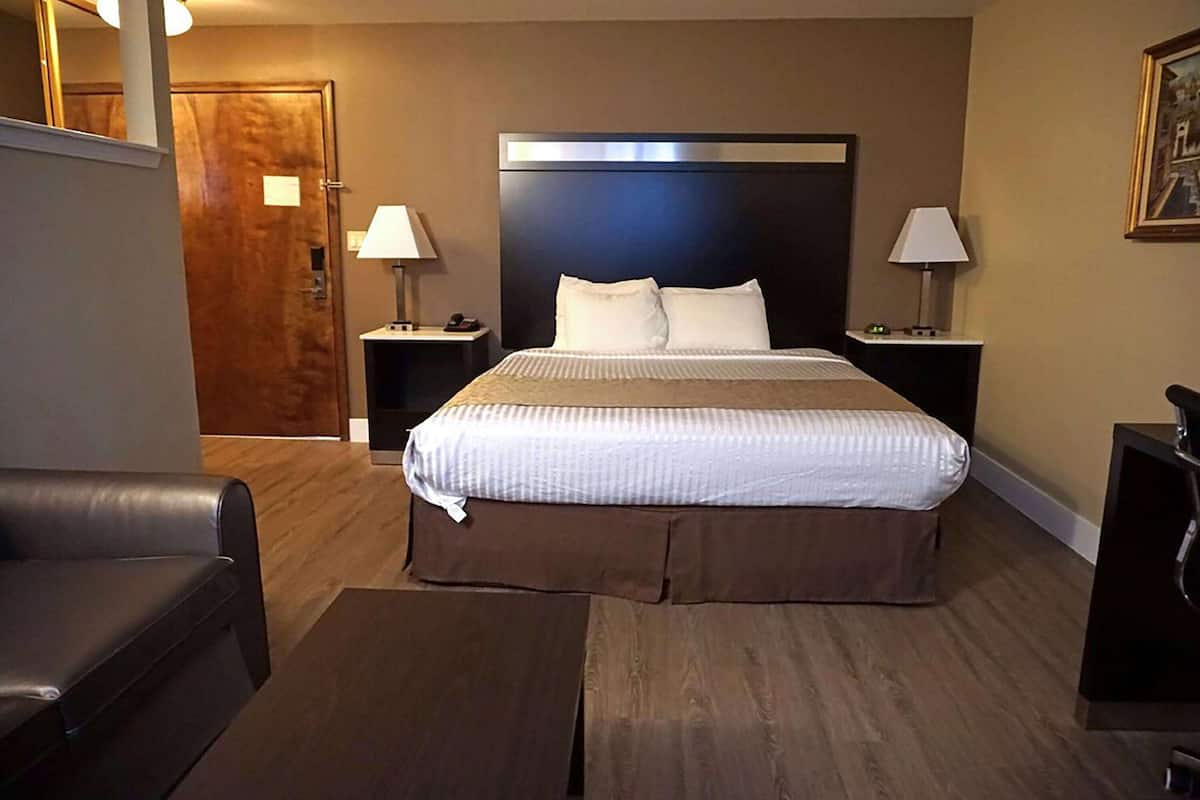A hotel room with a large bed, two bedside tables with lamps, a wooden floor, and a leather chair.