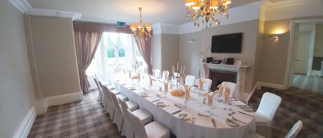 A formal dining room with a long table set for a meal, a chandelier, and a fireplace.